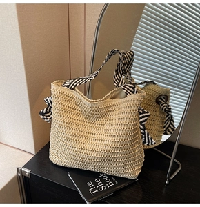 Detail of a straw woven tote bag featuring a black and white striped scarf handle and bow