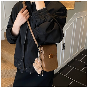 Detail view of retro brown crossbody phone bag with gold metal buckle and cute bear pendant