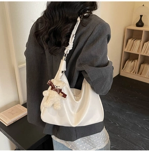 Detail of white moon-shaped hobo bag with a knotted strap and a cute plush bear charm