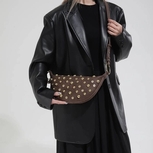 Close-up of a brown suede half-moon shoulder bag with gold metal studs and grommet details