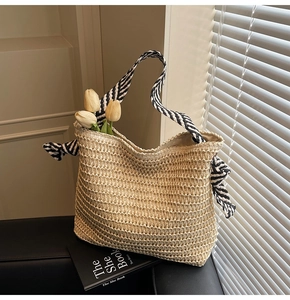 Close-up of beige woven straw tote bag with black and white striped fabric handles