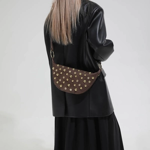 Detail view of a brown suede half-moon shoulder bag with gold rivets on a model