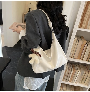 Detail view of white leather shoulder bag with knotted strap and cute plush bear charm