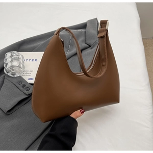 Détail d'un sac hobo croissant marron avec boucle argentée sur une veste grise
