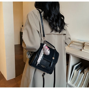 Detailed view of the black leather backpack featuring a gold logo and plush sheep charm