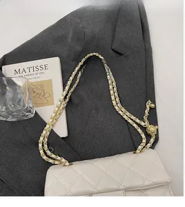 Detail of white quilted leather shoulder bag with gold chain and ball charm on grey suit