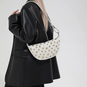 Detail of white half-moon shoulder bag with golden rivets and metallic ring hardware