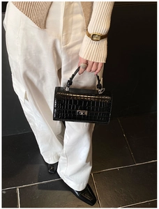 Detailed view of black crocodile pattern leather handbag with silver metallic turn-lock