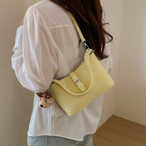 Pale yellow crossbody bag with leather texture and cute plush bear charm on a model
