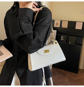 Détail du sac bandoulière en cuir verni blanc avec chaîne dorée et fermoir rotatif