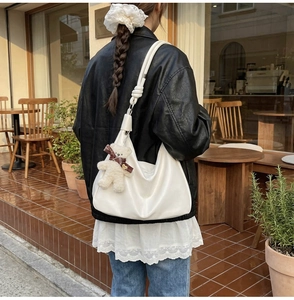 Side view of a white large hobo tote bag with a cute plush bear pendant in a cafe setting