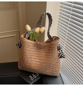 Detailed close-up of straw woven tote bag featuring black and white striped ribbon handles