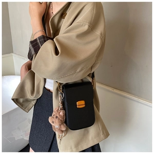 Detail of black mini crossbody bag with gold twist lock and cute brown bear charm accessory