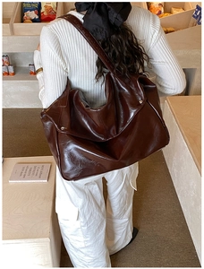 Detail view of a large dark brown leather tote bag worn as a crossbody for commute