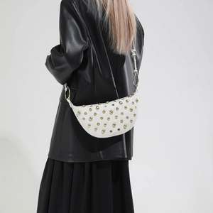 White crescent crossbody bag with gold rivet accents and slender shoulder strap