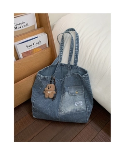 Detail of blue striped denim tote bag featuring front pocket and plush bear pendant