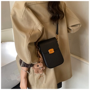 Detail view of black lychee grain crossbody phone bag with gold clasp and plush bear charm