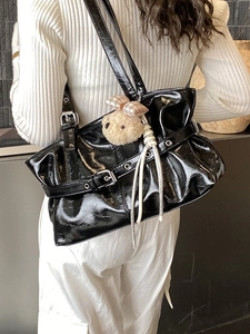 Large black glossy pleated tote bag with plush bear charm worn as a shoulder bag