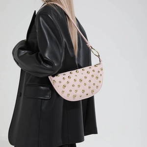 Close-up of light pink leather crescent bag with gold stud details on black blazer