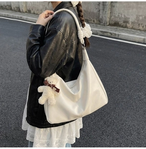 Close-up of a white leather tote bag featuring a knotted shoulder strap and plush bear charm
