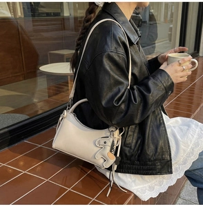 Detalle de bolso de cuero crema con colgante de caballo en modelo con chaqueta negra