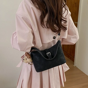 Detail of black suede shoulder bag with metal buckle and cute teddy bear charm