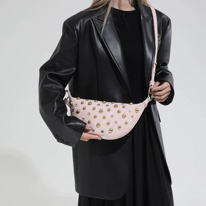 Detail of pink half-moon crossbody bag with gold rivets on a black leather blazer