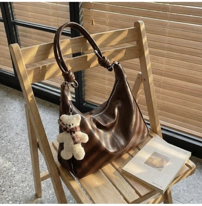 Detail of vintage dark brown hobo bag with teddy bear charm on a wooden chair