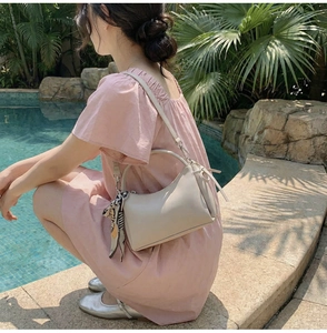 Bolso media luna beige con pañuelo floral mostrado por una modelo junto a una piscina
