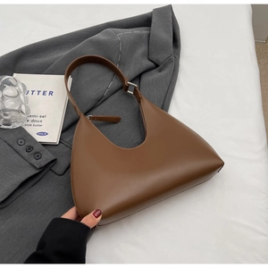 Détail d'un sac hobo marron foncé posé sur un blazer gris et un livre dans un décor lifestyle