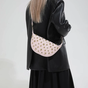 Pink crescent shoulder bag with gold studs on a model wearing a black leather jacket