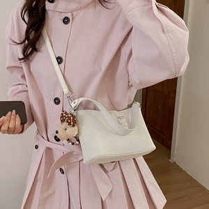 Detailed view of white faux leather crossbody bag with brown plush bear charm and metal clasp