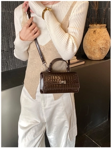 Detail of dark brown croc-effect leather handbag with gold metal lock and adjustable strap