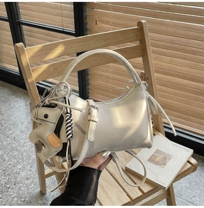 Detalle de un bolso de media luna blanco crema con colgante de caballo en silla de madera
