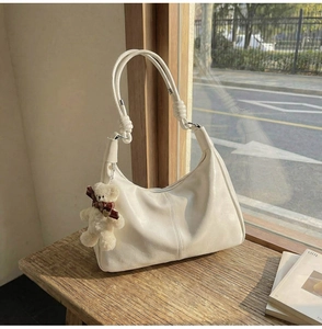 Close-up of cream PU leather tote bag with knotted handle and plush bear on wooden bench