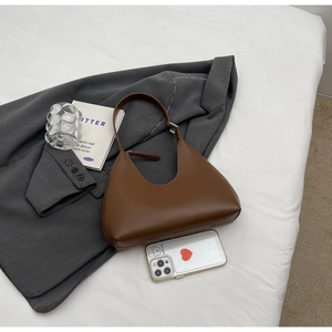 Détail d'un sac hobo marron foncé sur literie blanche avec accessoires de mode