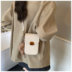Close-up of cream crossbody phone bag with gold clasp and brown teddy bear charm