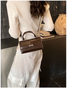 Detail view of dark brown crocodile embossed leather satchel with metal twist lock