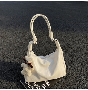 Detail of white leather shoulder bag featuring knotted handles and a cute plush bear charm
