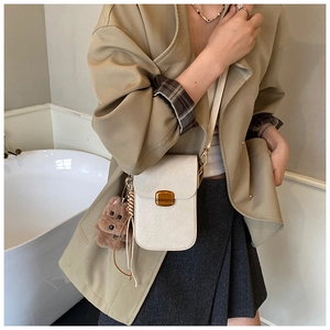 Detail of cream mini crossbody bag with golden lock and cute brown plush bear charm