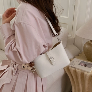 Close-up of white crossbody bag with decorative strap and a small brown bear plush charm