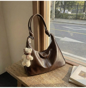 Detail view of dark brown leather tote bag with a cute plush bear charm on a wood bench
