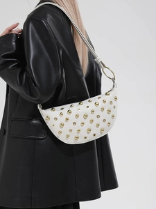 White crescent underarm bag with gold rivets and metallic eyelets on shoulder strap
