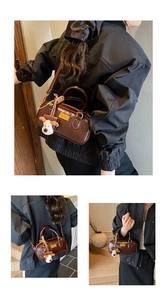 Detailed view of brown glossy Boston bag with white puppy plush charm and adjustable strap