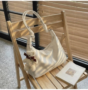Detail of off-white leather crescent bag with knot strap and plush bear charm on a chair