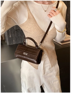 Detail of dark brown crocodile-embossed leather bag with silver buckle on cream top