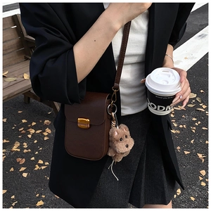 Detailed macro view of the dark brown leather grain and golden clasp on the shoulder bag