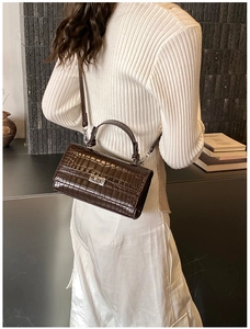 Detail view of deep brown crocodile embossed leather bag with golden metallic twist lock