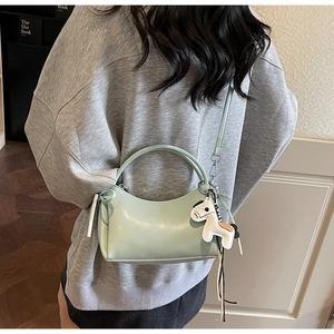 Detalle de bolso medialuna verde claro con colgante de caballo blanco y correa fina