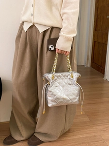 Sac seau matelassé argenté avec bandoulière chaîne dorée présenté dans un intérieur